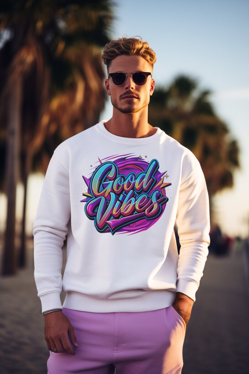 May include: A white sweatshirt with a colorful graphic print that says "Good Vibes". The person wearing the sweatshirt is wearing sunglasses and pink pants.