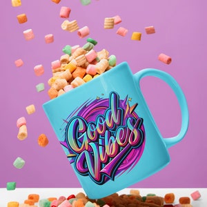 May include: A blue ceramic mug with the words "Good Vibes" in colorful lettering. The mug is filled with colorful cereal and the cereal is spilling out onto a white surface.