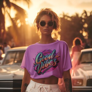 May include: A woman wearing a purple t-shirt with the text "Good Vibes" in colorful lettering. She is standing in front of a white car with palm trees in the background.