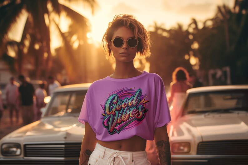 May include: A woman wearing a purple t-shirt with the text "Good Vibes" in colorful lettering. She is standing in front of a white car with palm trees in the background.