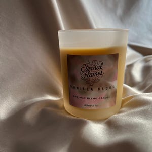 May include: A vanilla-scented soy wax blend candle in a frosted glass jar. The label reads "Eternal Flames Vanilla Cloud" with a pink and brown design. The candle is estimated to burn for 40 hours and is 28g.