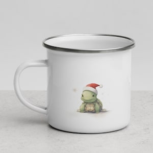 Könnte beinhalten: Weiße Emaille-Tasse mit einer grünen Schildkröte, die einen roten Weihnachtsmann-Hut trägt. Die Schildkröte sitzt auf einem weißen Hintergrund mit Schneeflocken.