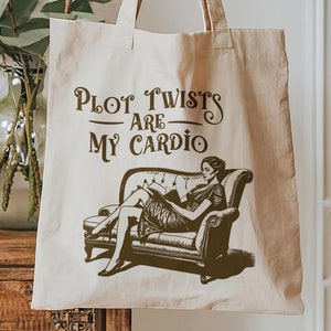May include: A beige tote bag with a brown graphic of a woman reading a book on a couch. The text "Plot Twists Are My Cardio" is printed on the bag.