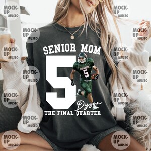 May include: Dark gray sweatshirt with the text "SENIOR MOM" above a large white number 5 and a football player graphic. The name "Dyson" and "THE FINAL QUARTER" are printed below the number. A casual, comfortable top.