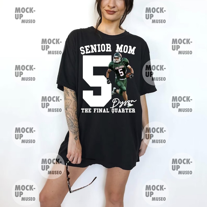 May include: Black t-shirt with the text "SENIOR MOM" above a large white number 5 and a football player graphic. Below the number is the name "Dyson" and the phrase "THE FINAL QUARTER" in white. The shirt is a casual style.