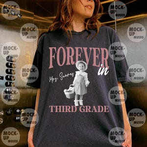 Może przedstawiać: Ciemnoszary t-shirt z czarno-białym zdjęciem małego dziecka w kapeluszu, trzymającego koszyk. Napis "FOREVER in Mrs. Suarez THIRD GRADE" wykonany jest dużymi różowymi i białymi literami na przedniej części odzieży.
