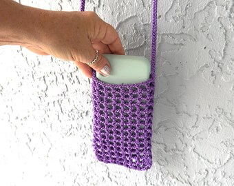 May include: Purple crocheted phone case with a light blue phone inside. The case is hanging from a purple crocheted strap.