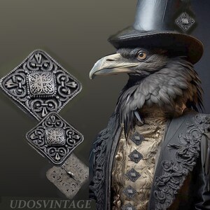 May include: A set of four silver-toned, ornate, square-shaped buttons with intricate designs. The buttons are arranged in a row on a gold fabric background. The buttons are surrounded by a black fabric with a decorative pattern.