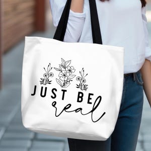 May include: White tote bag with black handles and the text "JUST BE real" in a stylised font. The text is surrounded by a floral design.