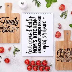 Könnte beinhalten: Drei Holzschneidebretter mit Text, umgeben von frischen Tomaten, Kräutern und Gewürzen. Auf einem Brett steht "Family gathers here", auf einem anderen "In this kitchen we count memories not calories", und ein Notizblock "love served daily."