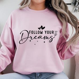 May include: Pink sweatshirt with the text "FOLLOW YOUR DREAMS" in black lettering with two small hearts and a floral design.