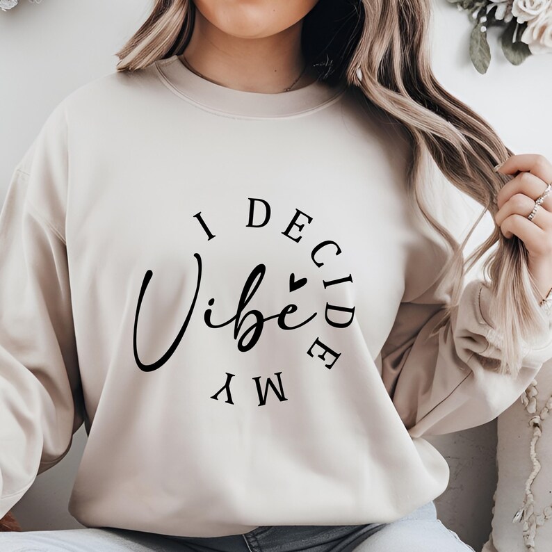 May include: A beige sweatshirt with the text "I Decide My Vibe" in black lettering.