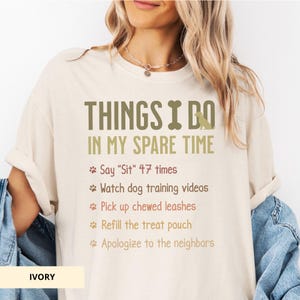 May include: Cream-coloured t-shirt featuring the text "THINGS I DO IN MY SPARE TIME." The list includes dog-related activities like saying "Sit" 47 times, watching training videos, and picking up chewed leashes.