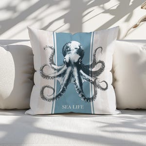 Könnte beinhalten: Ein weißes Kissen mit einem blauen Streifen und einer Schwarz-Weiß-Illustration eines Kraken. Das Kissen trägt den Text "SEA LIFE".
