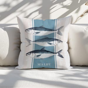 Könnte beinhalten: Ein weißes Kissen mit einem blauen Streifen in der Mitte und drei Schwarz-Weiß-Fischillustrationen. Der Text "SEA LIFE" ist unter den Fischen gedruckt.