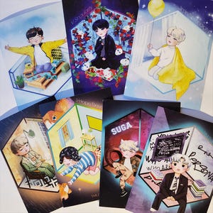 May include: A collection of colorful art prints featuring cartoon illustrations of figures in various settings. The prints have text such as "V Singularity", "Jimin Serendipity", and "SUGA". The artwork includes a variety of colors and styles.