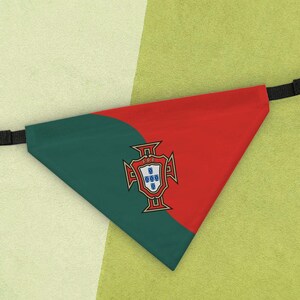 May include: A triangular pet bandana featuring the green and red colors of the Portuguese flag. The center displays the national coat of arms with the letters FPF. The bandana includes a black adjustable nylon strap with a plastic side-release buckle.