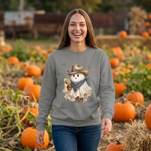 May include: A grey long-sleeve sweatshirt featuring a graphic of a ghost wearing a brown cowboy hat, a blue patterned bandana, and brown cowboy boots, while holding a glass with a straw, surrounded by small flying bats.