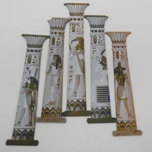 May include: Five decorative Egyptian-style columns with detailed illustrations of pharaohs and hieroglyphs. The columns are painted in shades of white, gold, and brown, with intricate designs at the top and base. The artwork evokes ancient Egyptian art.