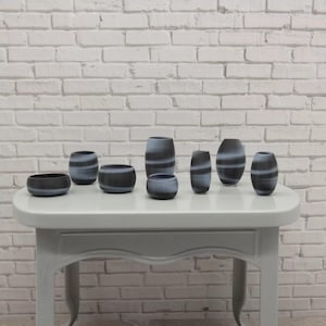 May include: A set of seven black and white striped ceramic vases and bowls of varying sizes. The vases and bowls are arranged on a light gray table.