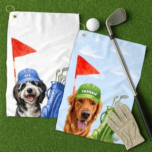 May include: Two golf towels with dog illustrations. One towel is white with a black and white dog wearing a blue cap that says "ACE". The other towel is blue with a golden retriever wearing a green cap that says "FRANKIE". A golf ball, club, and glove are also present.