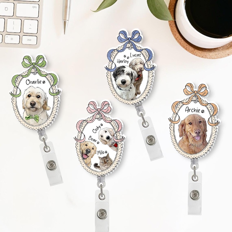 May include: Four personalised pet ID badge reels featuring different dog breeds and a cat, each with a name. The badges have a decorative oval frame with a bow at the top and a retractable reel clip.