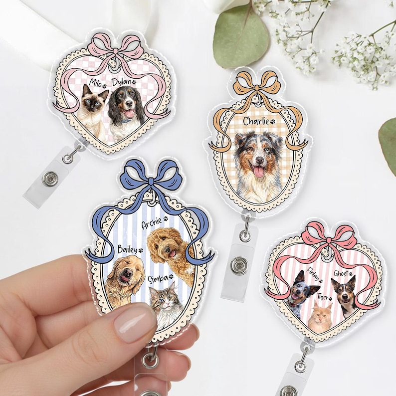 May include: A collection of personalized pet ID badge reels. Each reel features a pet portrait within a heart-shaped frame, adorned with a ribbon and the pet's name. The reels showcase various dog and cat breeds, with a clear plastic finish.
