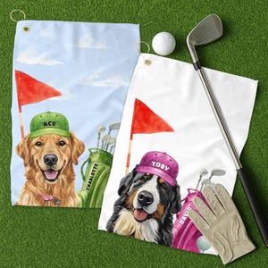 May include: Two golf towels with dog portraits. One features a golden retriever wearing a green cap with "ACE" on it, the other a Bernese Mountain Dog in a pink cap with "TOBY". Golf clubs, a golf ball, and a golf glove are also visible.