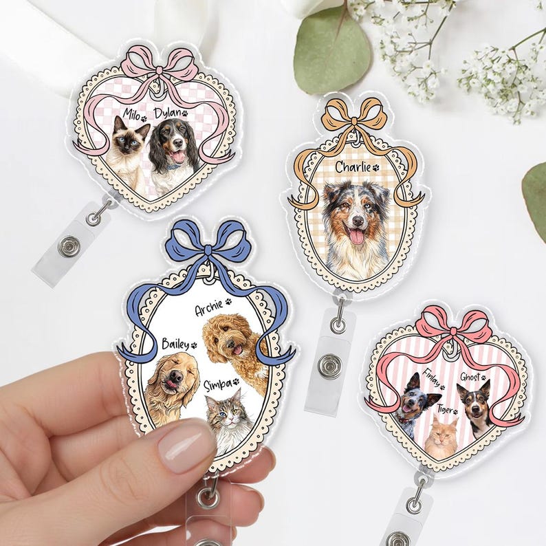 May include: Custom pet portrait badge reels with illustrations of dogs and cats. Each reel has a unique design with a bow and the pet's name. The reels are in various colors, including pink, blue, and gold.