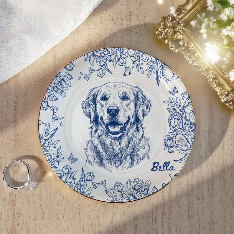 May include: White ceramic plate with a blue floral border and a detailed illustration of a Golden Retriever's face. The dog's name, "Bella," is written in cursive. The plate has a gold rim.
