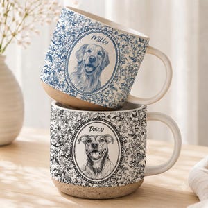 May include: Two ceramic mugs with a speckled tan base and a floral pattern. The top mug is blue and white with a portrait of a dog labeled Milly. The bottom mug is black and white with a portrait of a dog labeled Daisy. Both feature a central oval frame.