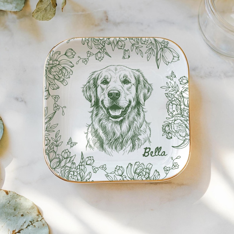 May include: Square white ceramic dish with a gold rim, featuring a detailed green sketch of a Golden Retriever dog. The dog's name, "Bella," is written in script. Floral and butterfly designs frame the dog portrait.