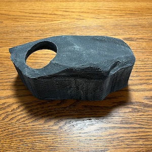 May include: A dark gray, textured, 3D printed rock with a round hole in the center. The rock is designed to be used as a hideaway for small animals.