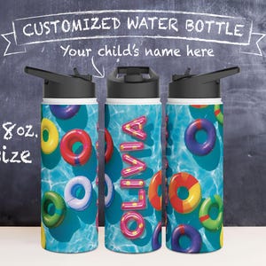 May include: A white water bottle with a blue and green pool design and colourful inflatable rings. The bottle has a black lid and a flip top spout. The name "Olivia" is printed in pink letters on the bottle. The bottle is 18 oz. in size.