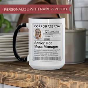 Puede incluir: Taza de cerámica blanca con asa y borde negros. La taza presenta un diseño personalizado con una foto y el texto "CORPORATE USA" y "Senior Hot Mess Manager". La taza está sobre una superficie de madera.