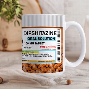 May include: White ceramic mug with a humorous design that looks like a prescription bottle label. The label reads "Dipshitazine Oral Solution 100 mg Tablet" with the text "QTY: 90" and "CWS Pharmacy Prescriber: Dr. Popem". The label also includes the instructions "Take as needed when dealing with an excess of stupidity."