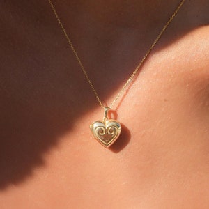 May include: A gold chain necklace with a heart-shaped locket pendant. The locket has a delicate, ornate design.