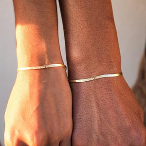 May include: Two gold bracelets with the words "Right With You" engraved on them. The bracelets are worn on the wrists of two people.
