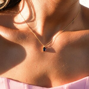 Peut inclure: Un collier en chaîne dorée avec un pendentif en forme de larme orné d'une pierre précieuse bleu foncé.