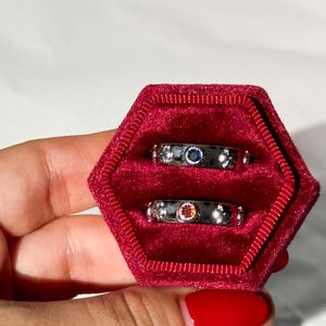 May include: Two silver rings with colorful gemstones set in a red velvet ring box.