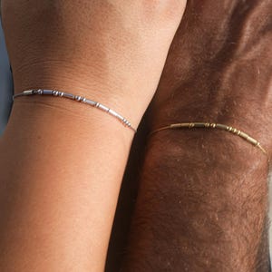 May include: Two bracelets on wrists, one silver and one gold, with small beads.