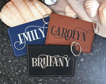 May include: Three leather keychains with silver key rings. The keychains are navy blue, brown, and black. Each keychain has a name engraved in silver lettering: Emily, Carolyn, and Brittany.