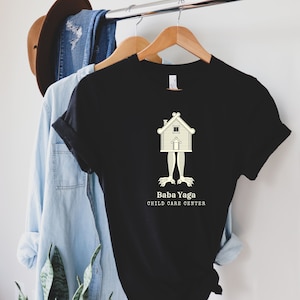 ババ・ヤガ チャイルドケアセンター Tシャツ、面白い魔女シャツ、ハロウィンシャツ、フォークロアシャツ、魔術シャツ、プレミアムユニセックスクルーネックTシャツ