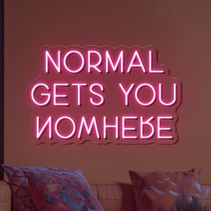 Könnte beinhalten: Rosa Neon-Schild mit dem Text "NORMAL GETS YOU NOWHERE" an einer Wand in einem Wohnzimmer mit einer Couch und einer Pflanze.