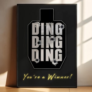 Könnte beinhalten: Ein schwarz-weißes Poster mit einer Zielscheibe und dem Text "DING DING DING" in silberner Schrift. Die Zielscheibe hat Einschusslöcher und der Text "You're a Winner!" befindet sich unterhalb der Zielscheibe in Gelb.