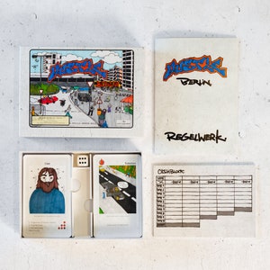 May include: A board game called "Hustle Berlin" with a colorful illustration of a city street scene on the box lid. The game includes a cash block, dice, and cards with illustrations of people and places.
