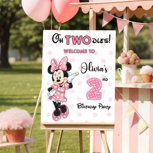 May include: A rectangular birthday party welcome sign on a wooden easel featuring a pink polka dot background, an illustration of Minnie Mouse, and the text: Oh TWOdles! Welcome to Olivia's 2nd Birthday Party. The sign is displayed outdoors.