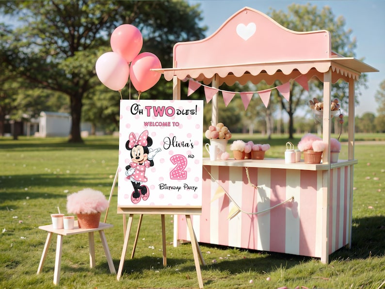 May include: A rectangular birthday party welcome sign on a wooden easel featuring a pink polka dot background, an illustration of Minnie Mouse, and the text: Oh TWOdles! Welcome to Olivia's 2nd Birthday Party. The sign is displayed outdoors.