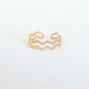 Op de afbeelding: Een goudkleurige ring met een dubbellaags zigzagontwerp. De ring heeft een reeks kleine, gelijkmatig verdeelde kralen langs de randen, waardoor een textuur ontstaat. Het open ontwerp maakt maatverstelling mogelijk. De ring staat tegen een witte achtergrond.