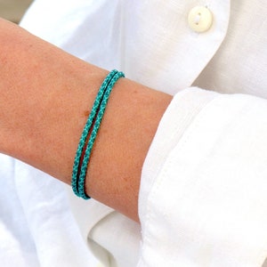 Peut inclure: Un bracelet turquoise à deux brins est porté sur un poignet, sur une chemise blanche. Le bracelet est fait d'un matériau tissé. La chemise a un poignet boutonné et un col boutonné.